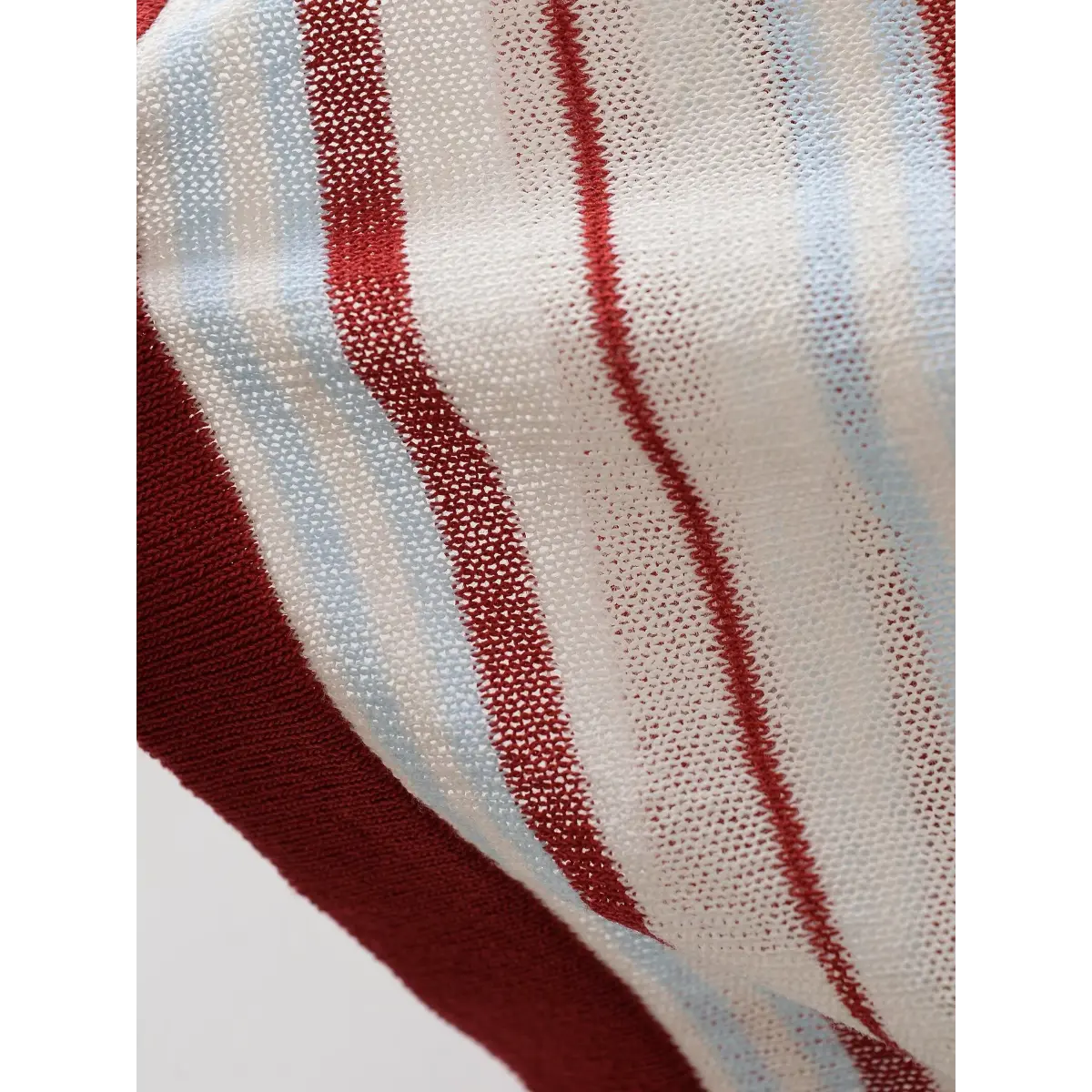 Close-up of the semi-sheer mesh fabric on the red and light blue striped knit top, highlighting the open-knit texture