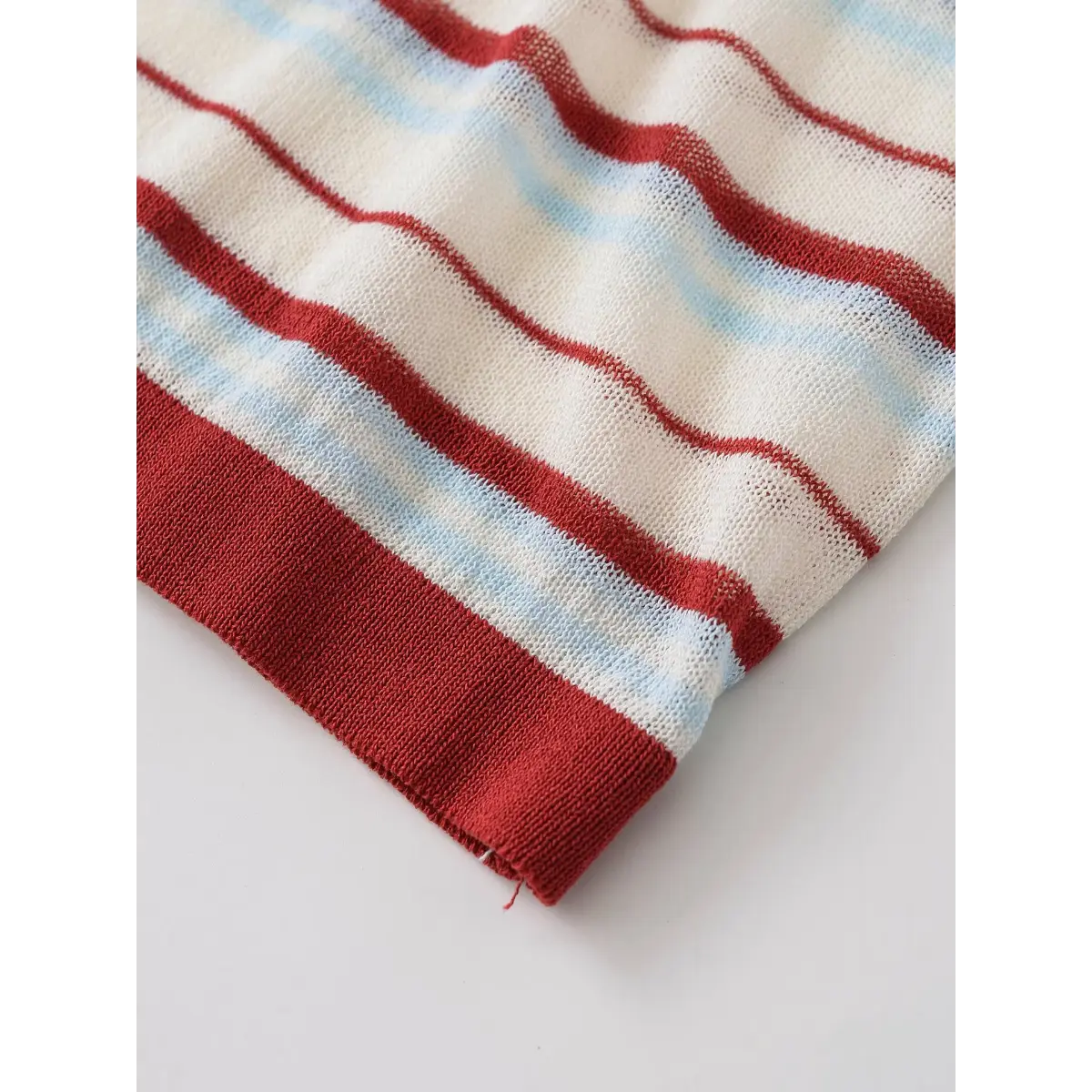 Close-up of the ribbed hem on the red and light blue striped knit top, showing the finish and stripe pattern
