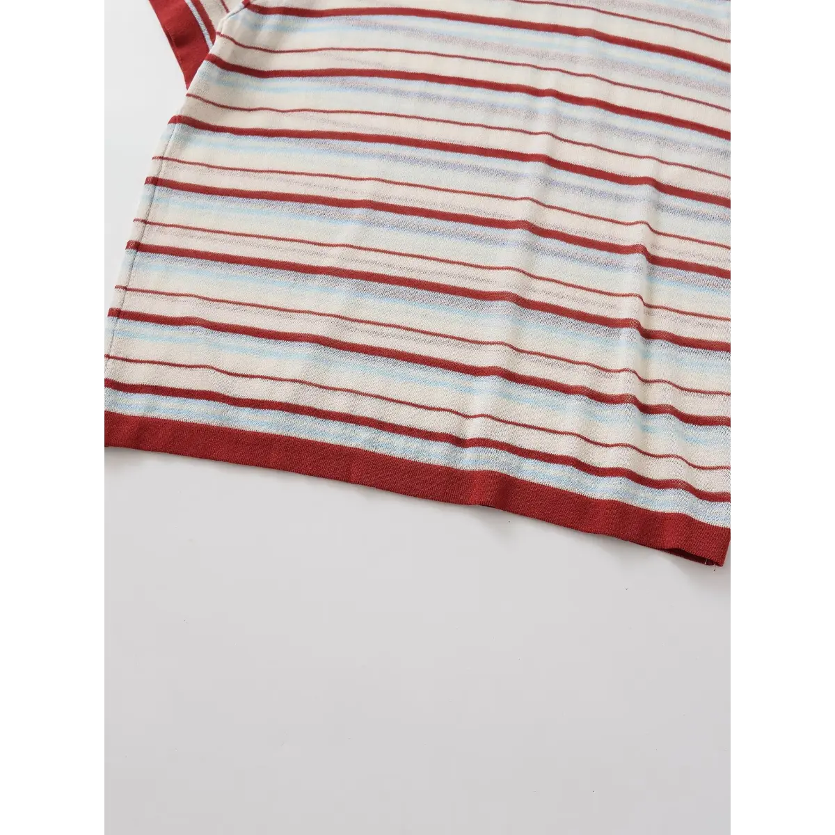 Hem detail of the red and light blue striped knit top, showing the ribbed trim and even stripe pattern