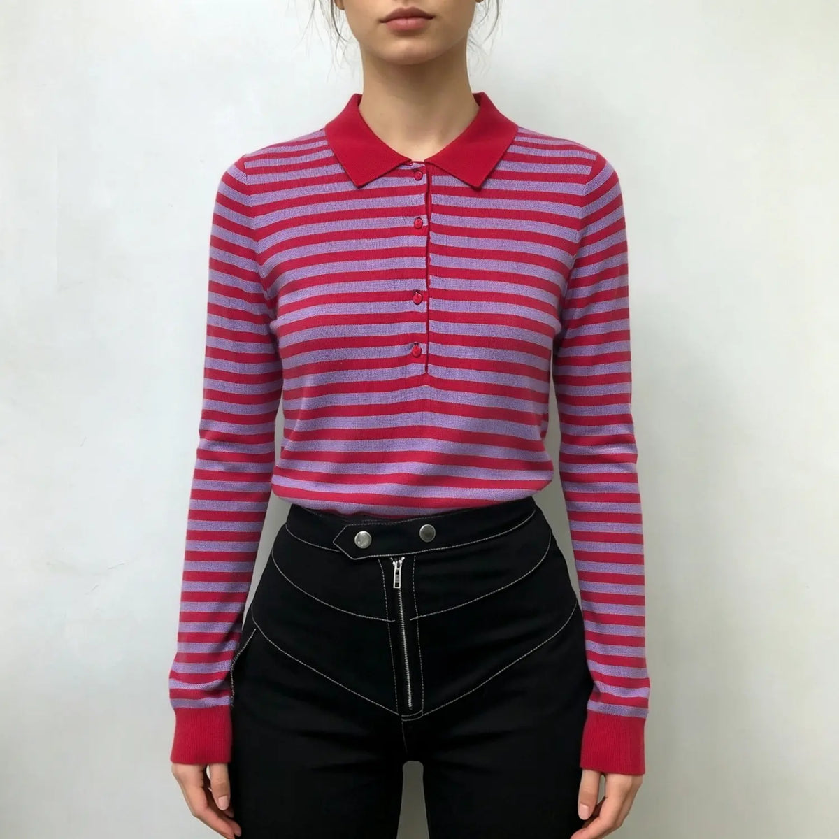 Model wearing striped polo knit top with red collar and buttons, paired with black pants on white background