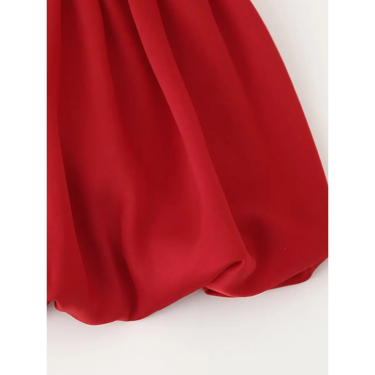 Close-up of the peplum hem on the red cami top, showing the rounded bubble silhouette and smooth fabric