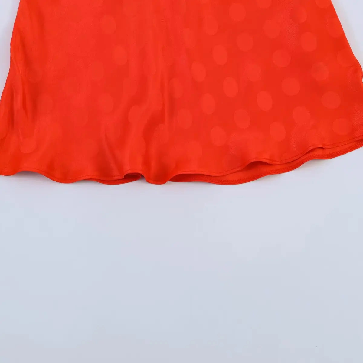 Hem detail of the red polka dot jacquard dress, showing the flared edge and fabric texture