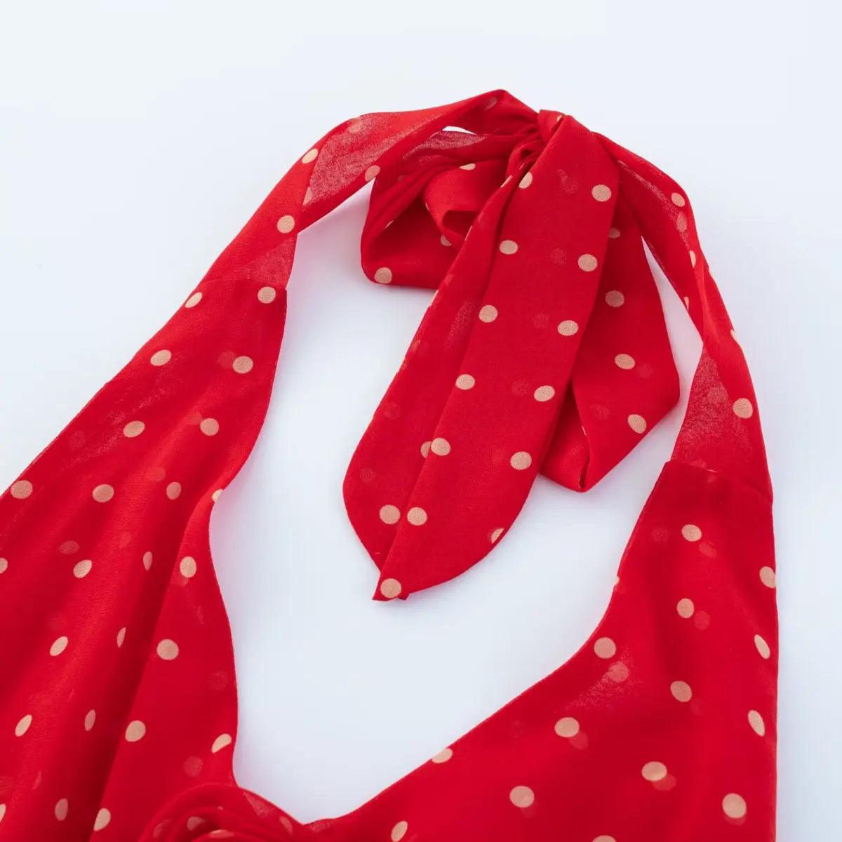  Close-up of self-fabric halter neck tie bow on red chiffon polka dot dress, lightweight sheer fabric texture.