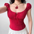 Front view of a woman in a red polka dot puff sleeve top, featuring a sweetheart neckline, red ribbon tie, and lace underbust detail.