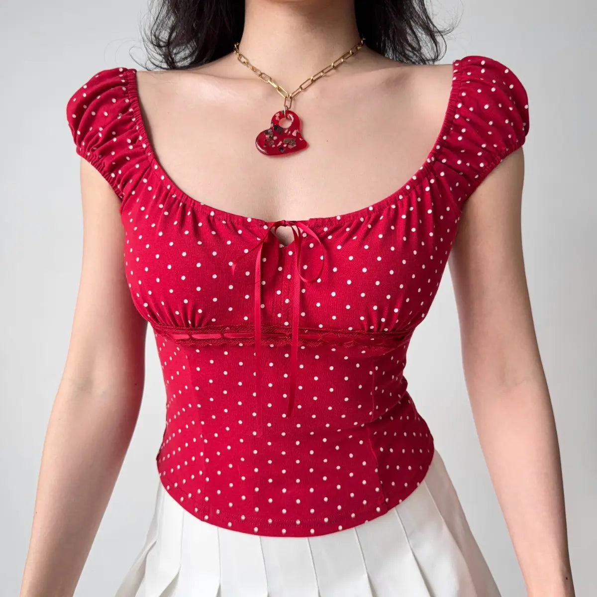 Woman wearing a form-fitting red polka dot top with puff sleeves, square neckline, and red ribbon tie detail at the bust.