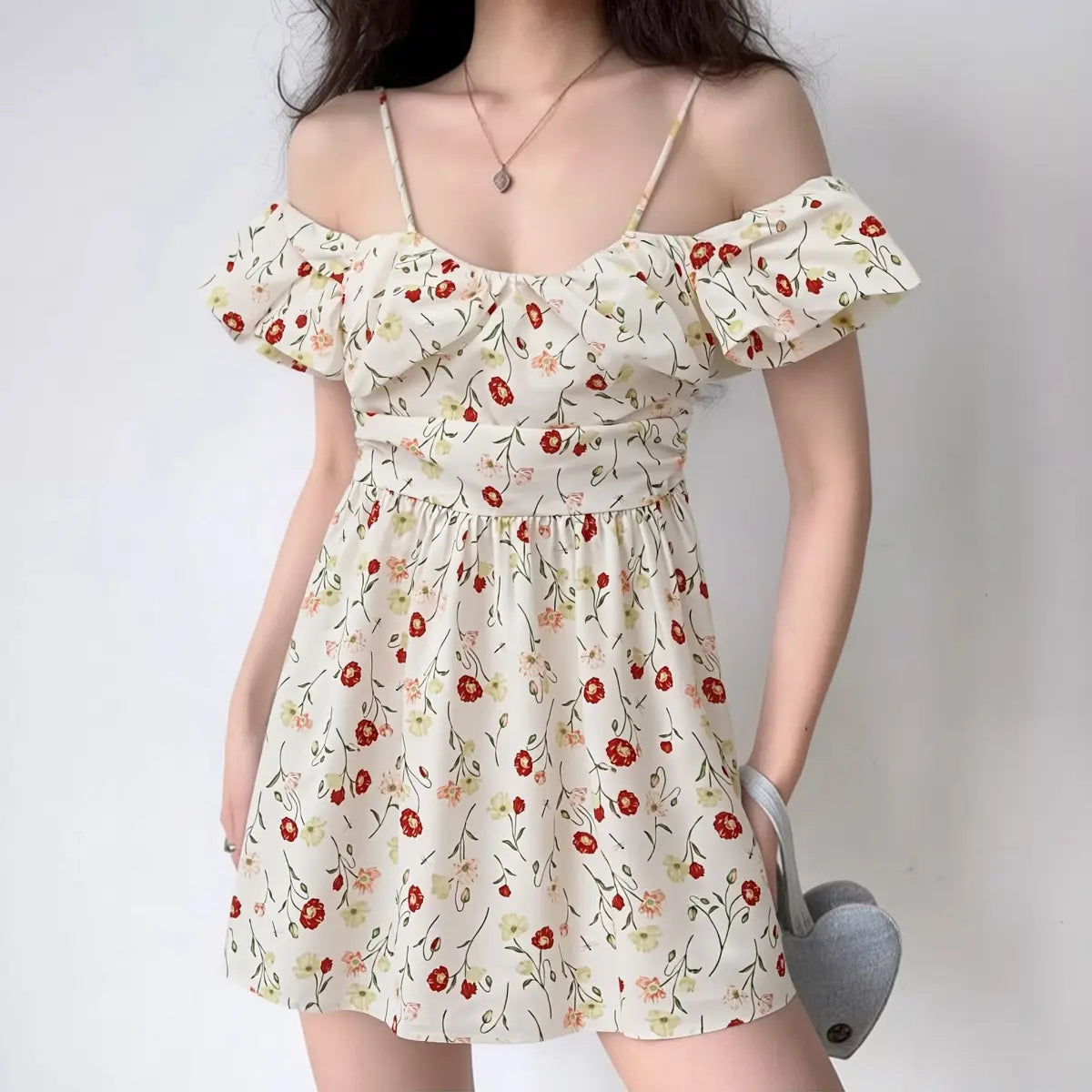 Model wearing a white poppy-print off-shoulder mini dress with puff sleeves and spaghetti straps.