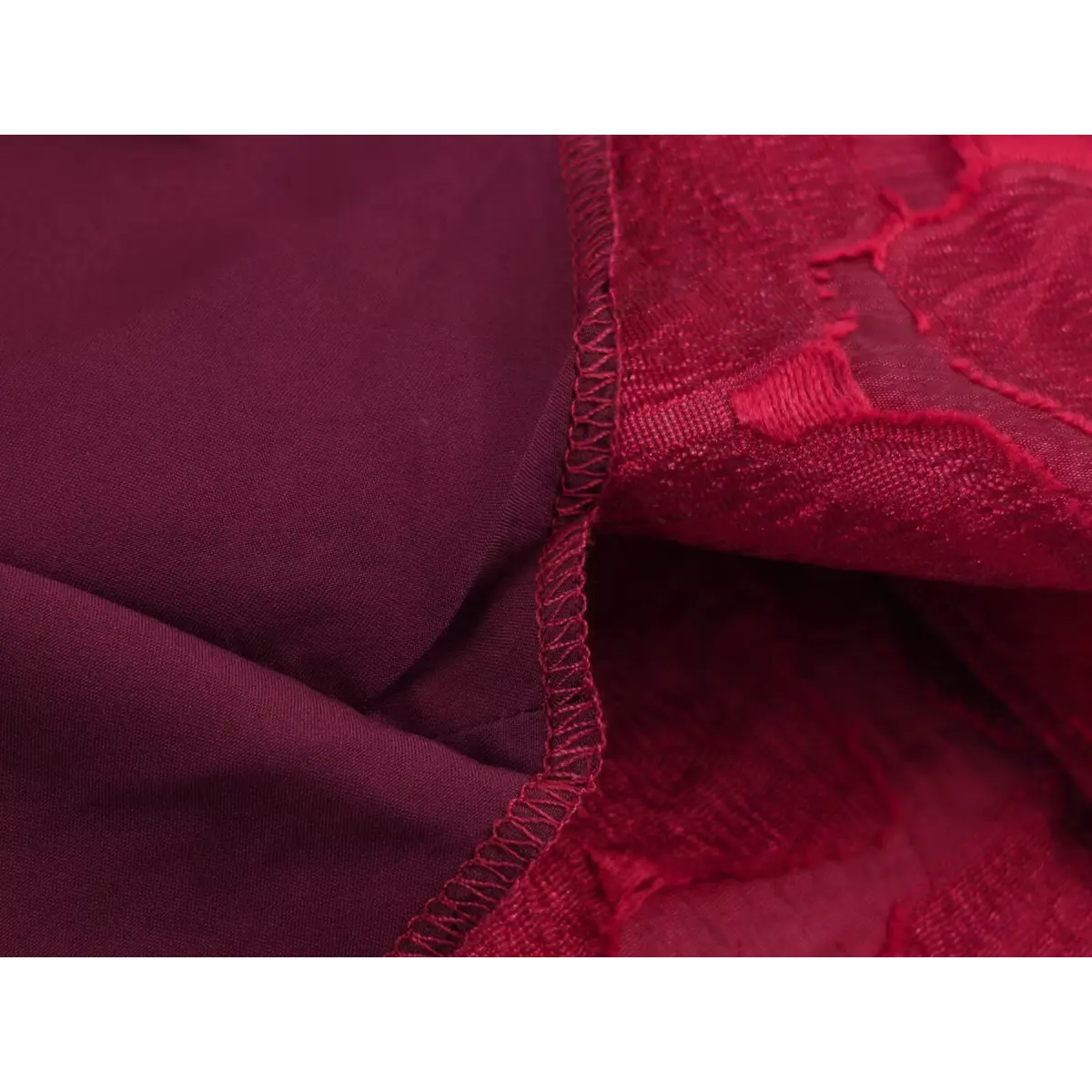 Close-up of the lining, overlock seam, and textured rose brocade fabric on a red sleeveless dress.