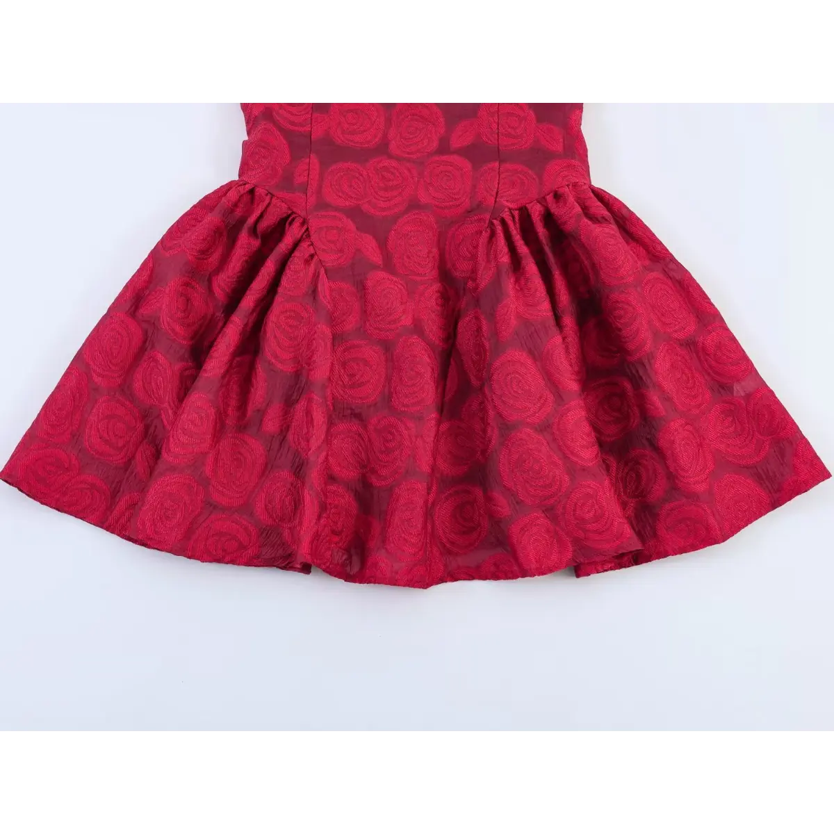Close-up of the gathered skirt on a red rose brocade sleeveless dress, showcasing the rose pattern and flowy silhouette.