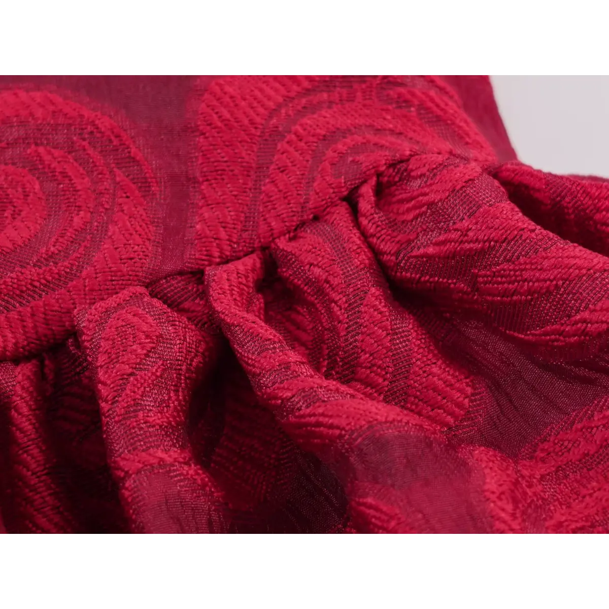 Macro close-up of the gathered skirt fabric on a red rose brocade dress, highlighting the embossed rose pattern.
