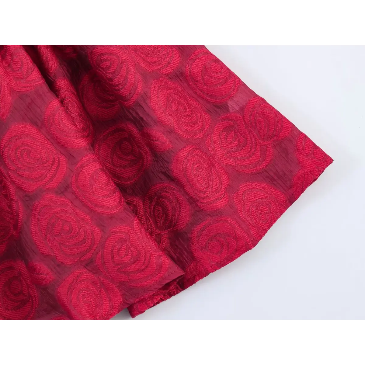 Close-up of the skirt hem and rose brocade fabric texture on a red sleeveless dress.