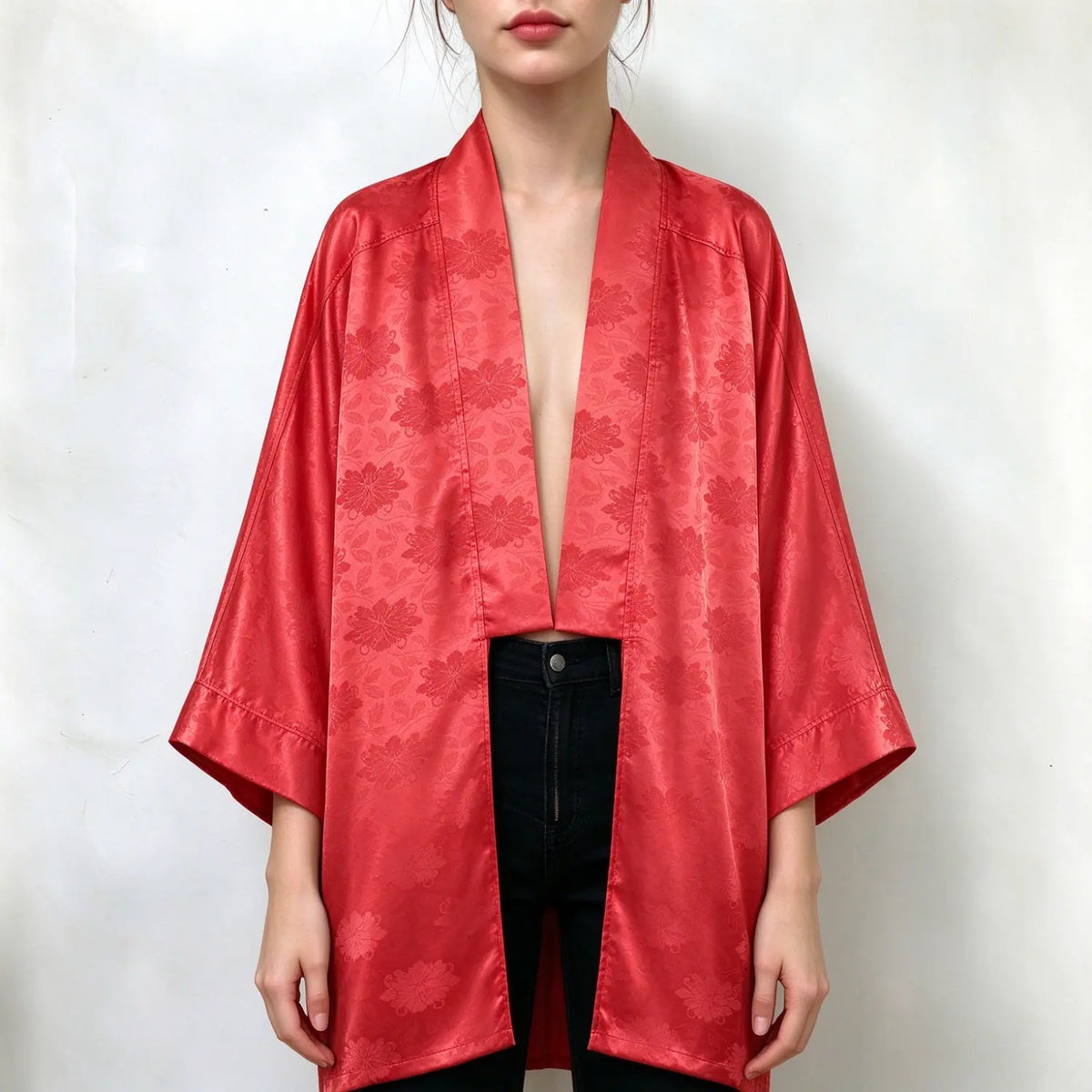 Model wearing red satin kimono cardigan, subtle floral jacquard pattern, open front, wide three quarter sleeves, loose relaxed fit, paired with black jeans, plain white background