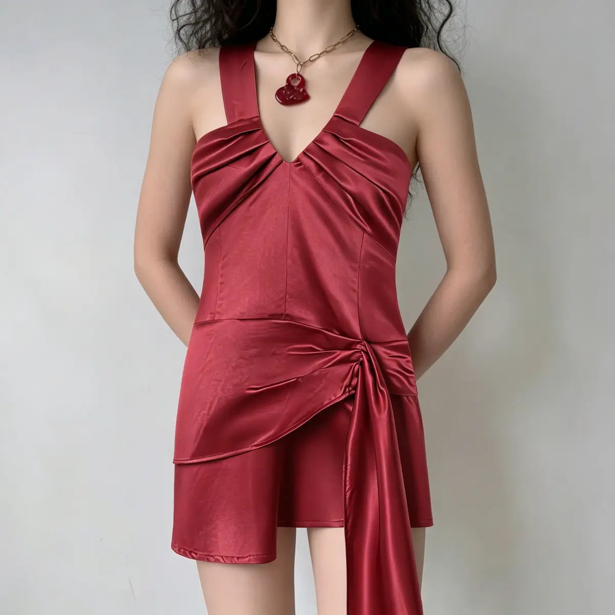 Model wearing a red satin wide-strap mini dress with V-neck, side tie detail and draped sash, styled with a red pendant necklace, back view.