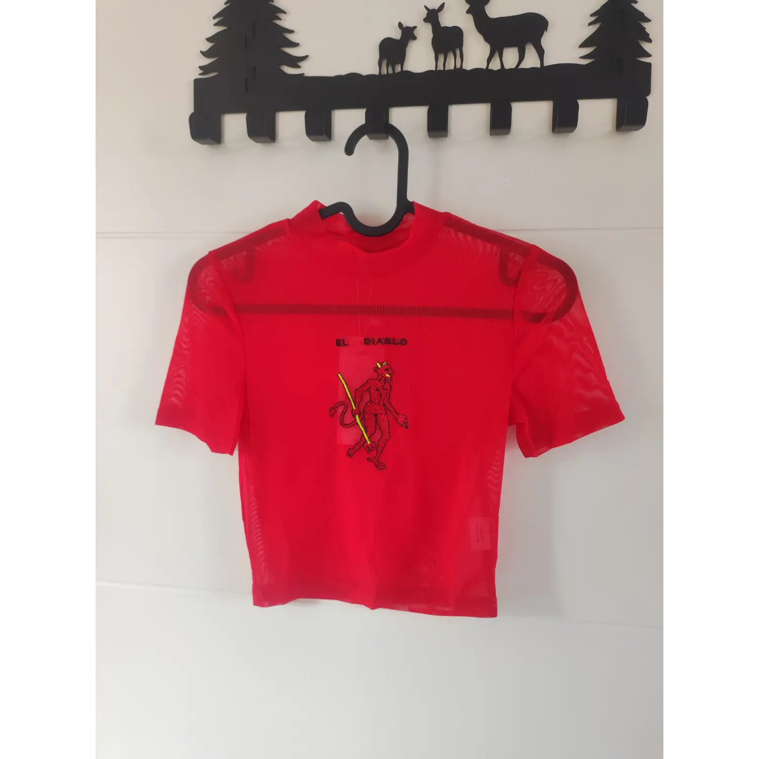 Wall hanging front view, red mesh mock neck cropped t-shirt with EL DIABLO graphic embroidery