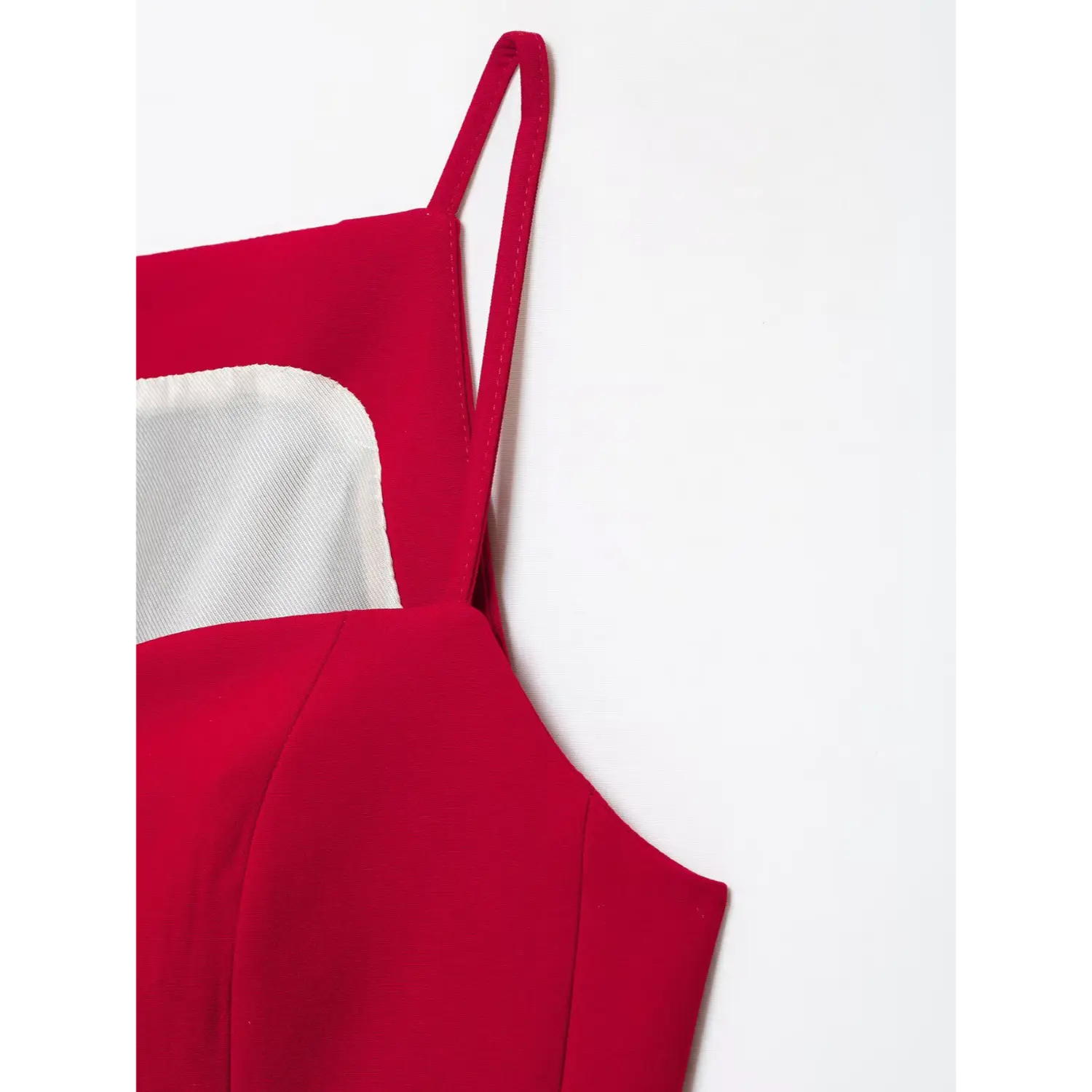 Close‑up side shoulder view of red tailored cami top, thin spaghetti strap, stitching seam detail, structured suiting fabric, white background