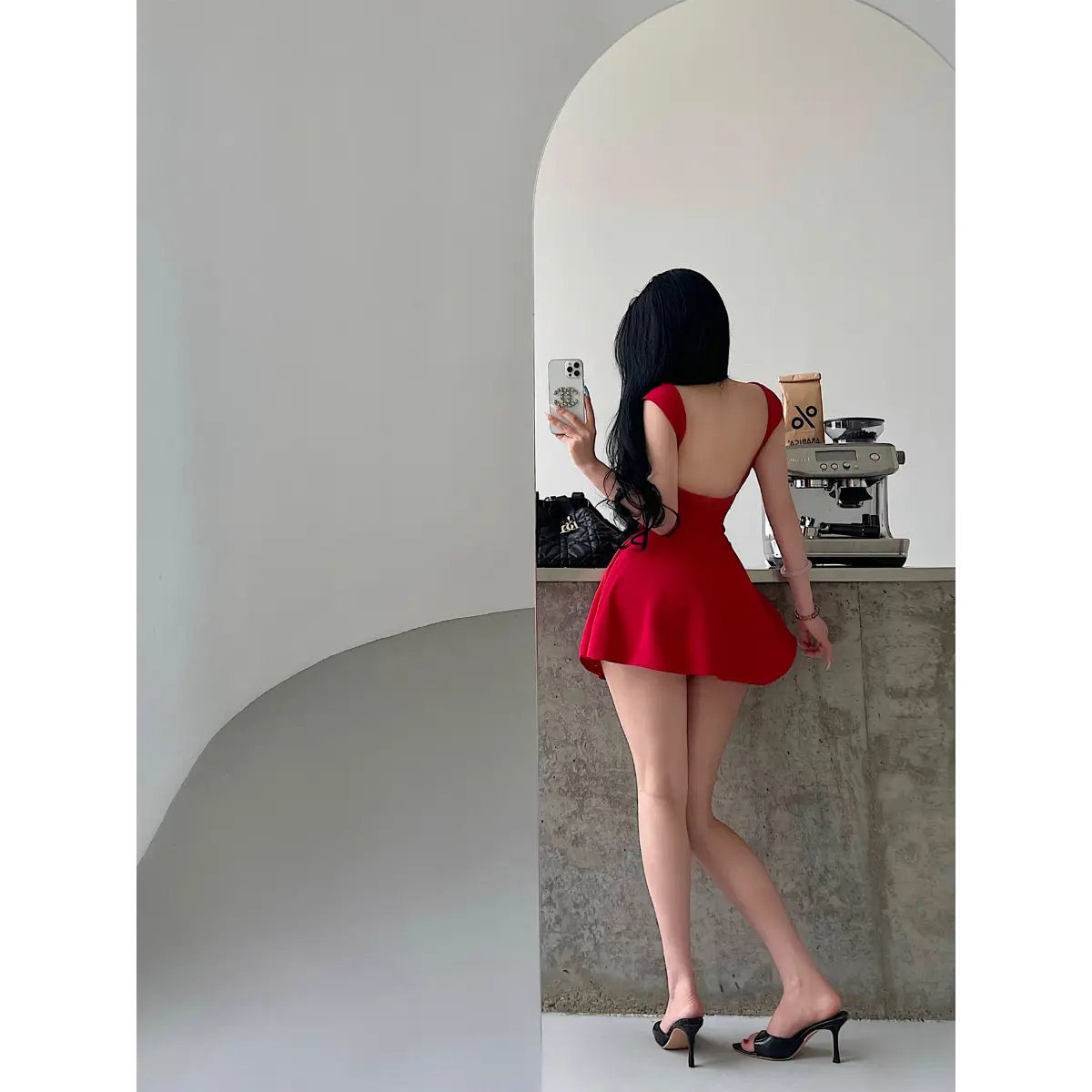 Back view of a woman wearing a bright red square-neck, low-back fit-and-flare mini dress taking a mirror selfie.