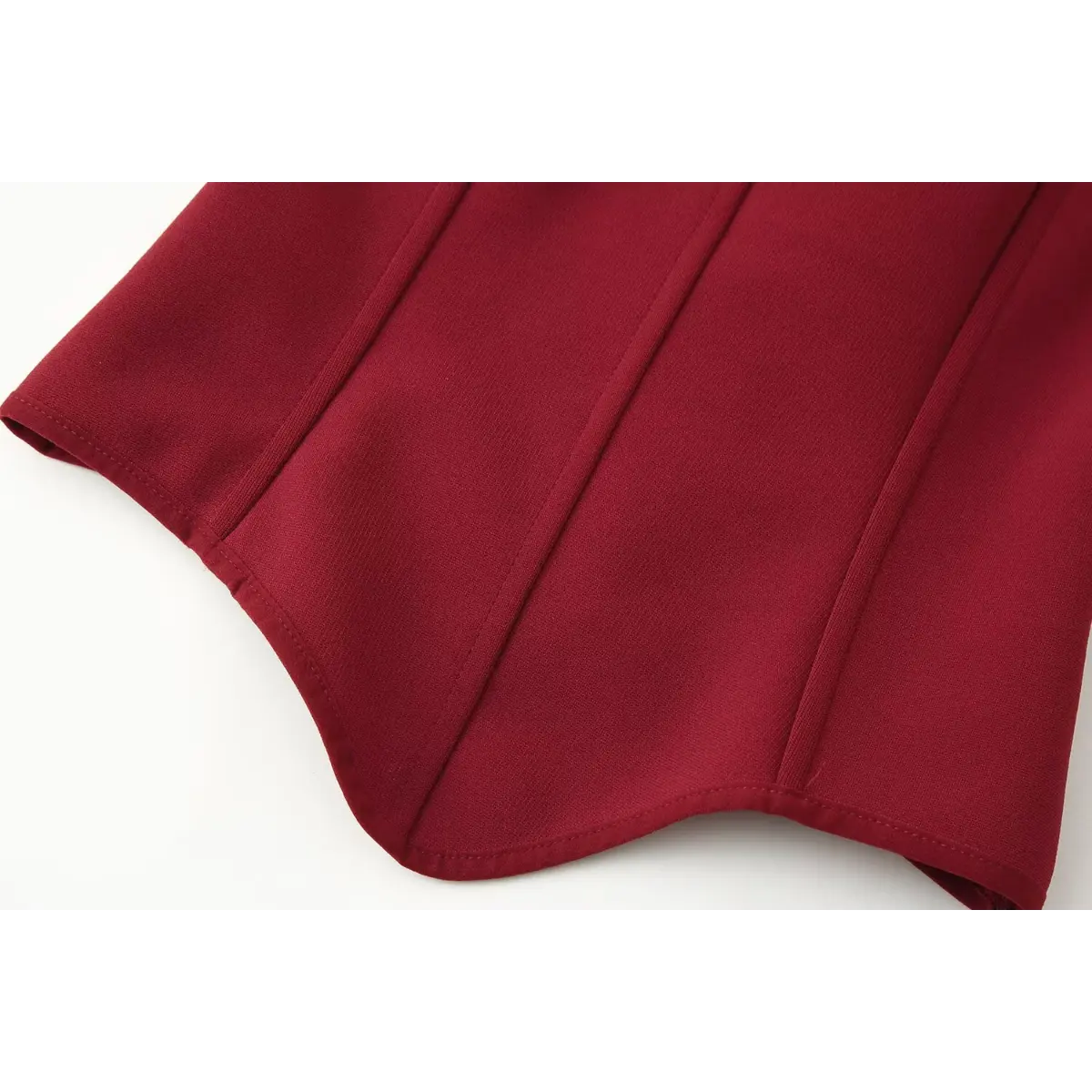 Close-up of the curved hem on the red bustier cami top, showing the structured vertical seams and clean edge