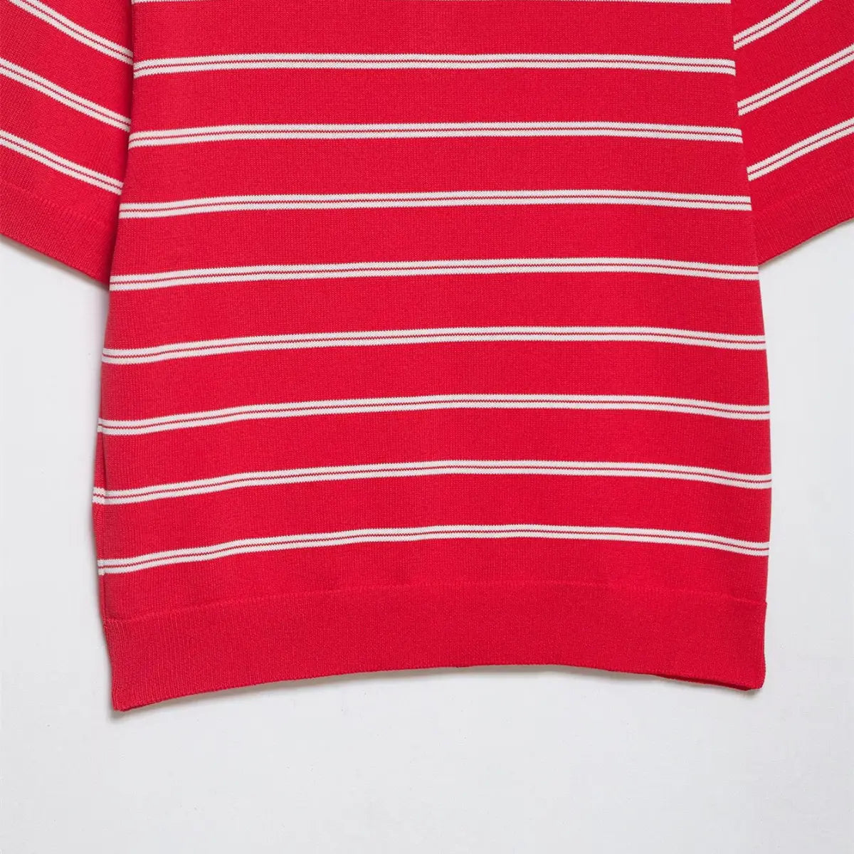 Close-up of the lower hem on the red and white striped knit polo shirt, showing the ribbed finish and horizontal stripe pattern