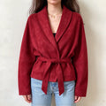 Female model wears red faux suede wrap jacket, shawl lapel collar, self tie waist belt, relaxed long sleeves, front torso shot