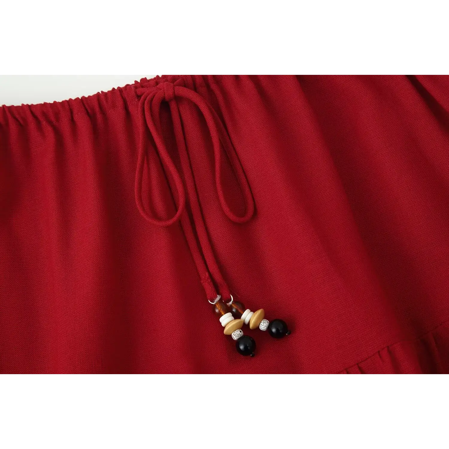 Close‑up of red tiered maxi skirt elastic waist with decorative multi‑color beaded drawstring tie, woven fabric texture