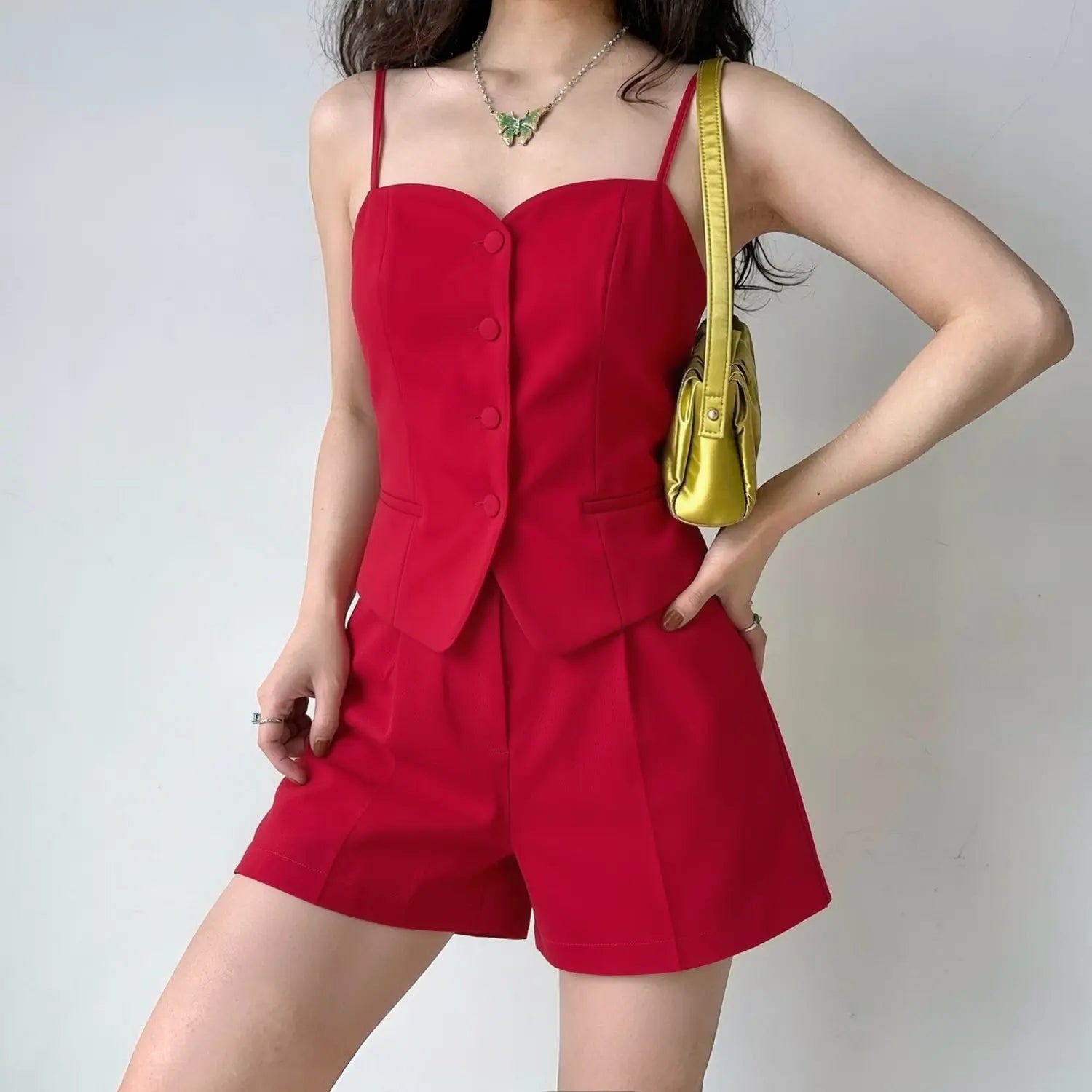 Model wearing red two‑piece suit set, heart neck spaghetti strap cami vest top and high‑waist pleated tailored shorts, studio plain grey background