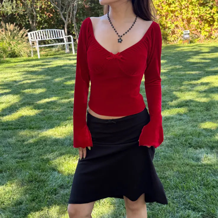 Model wearing red velvet sweetheart bow long sleeve crop top with black skirt, park view