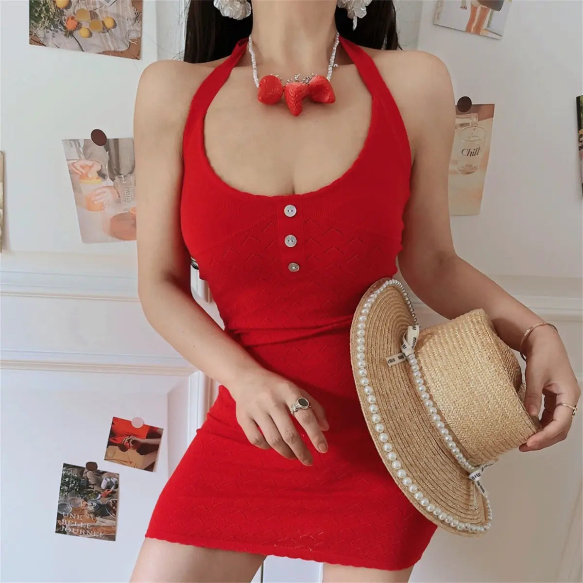 Full front indoor lifestyle photo of bright red hollow knit halter wrap mini dress, matched with pearl-trim straw hat, sweet vacation style.