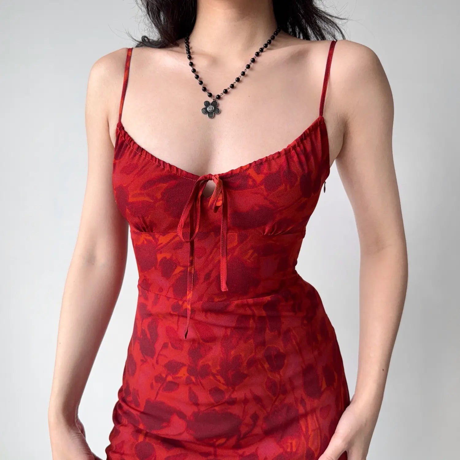 Close-up of the ruffled V bust with center tie knot, thin adjustable shoulder straps and layered red floral print texture
