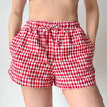 Lifestyle shot of red and white gingham shorts, with hands inserted into the side pockets