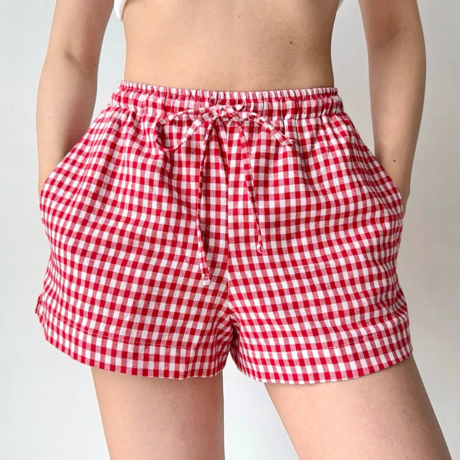 Lifestyle shot of red and white gingham shorts, with hands inserted into the side pockets