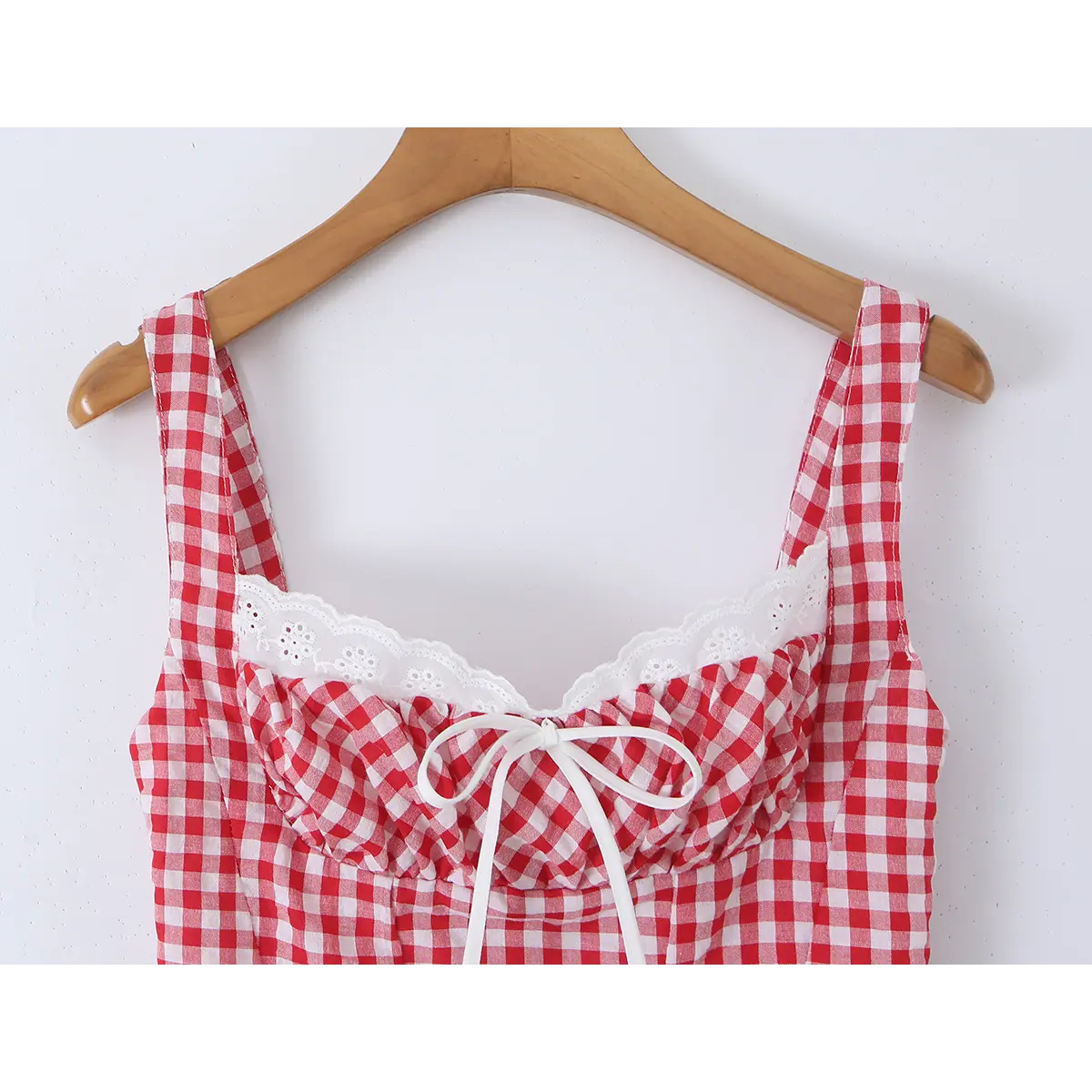 Close-up of a red and white gingham bustier tank top hung on a wooden hanger, showing the lace-trimmed scalloped neckline, center bow, and gathered bust detail.