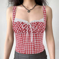 A woman wearing a red and white gingham bustier tank top with lace trim, center bow, and corset-style silhouette, styled with a black flower necklace and gray bottoms.