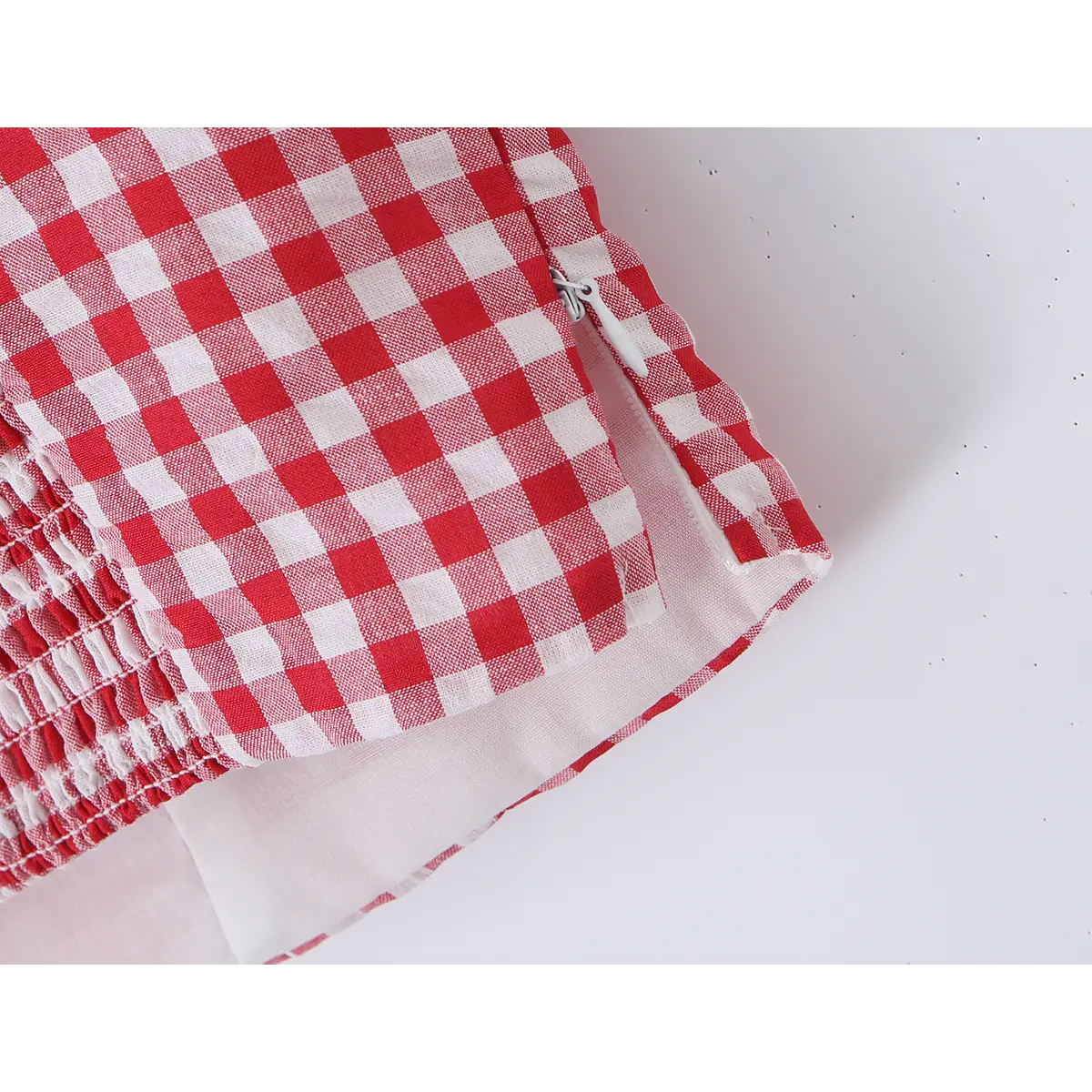 Close-up detail of the side zipper on a red and white gingham bustier tank top, showing the invisible zipper and fabric construction.
