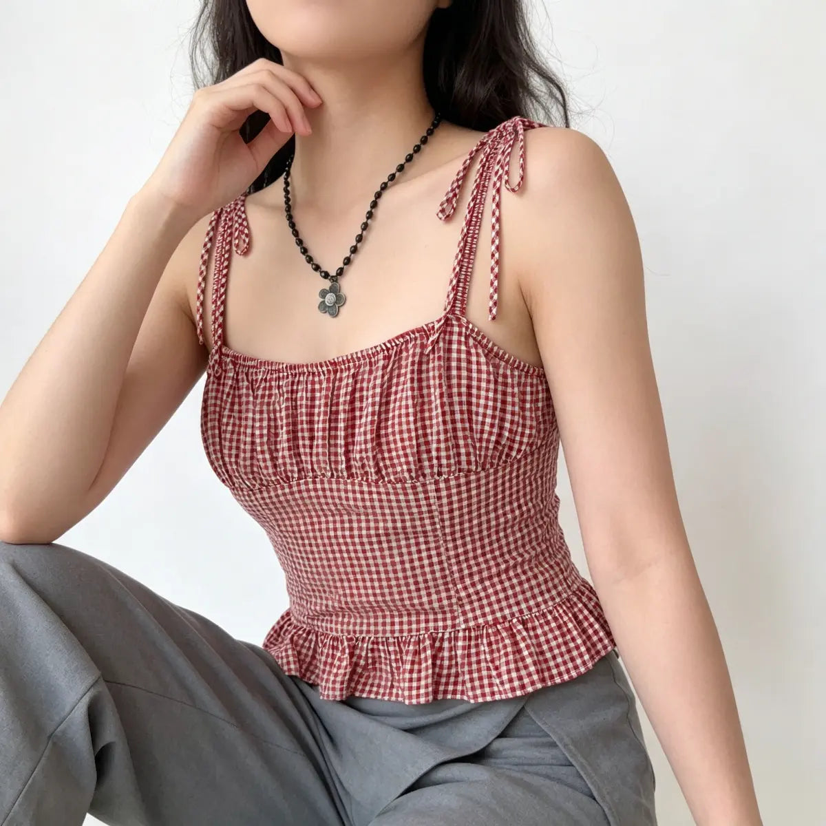 Slight angle view of a red and white gingham cami top with tie straps and ruffled hem.