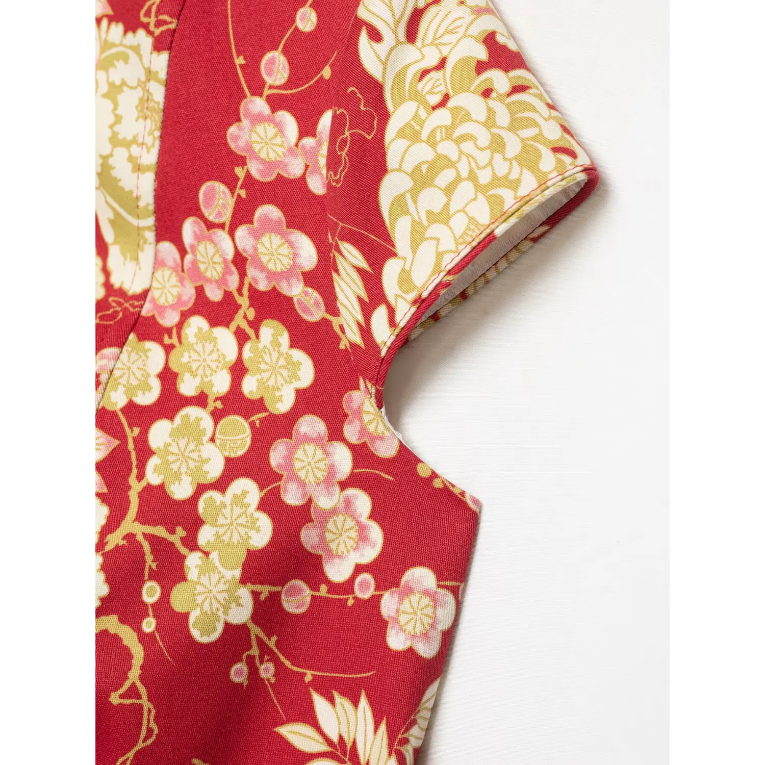 Close‑up of cap sleeve armhole seam and vivid red peony‑plum floral printed fabric