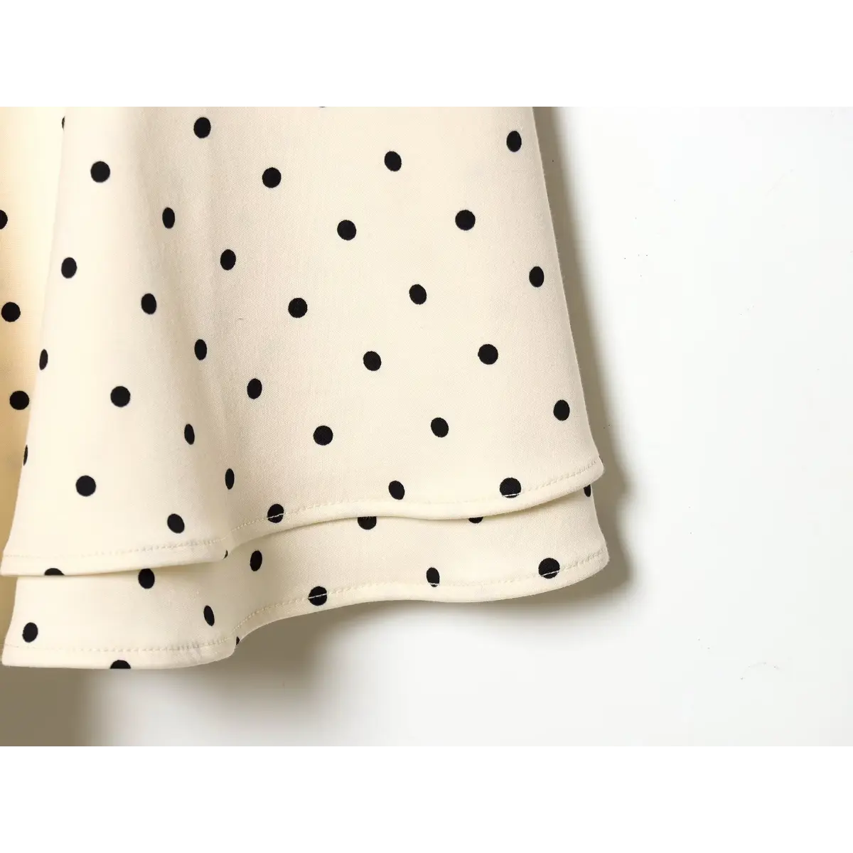 Macro fabric detail of black dot on off-white twill material, double tier ruffle skirt edge with clean overlock seam.