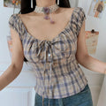Vintage purple plaid fitted short top, square neck tiny puff sleeve button front, full front shot against white wall with printed posters
