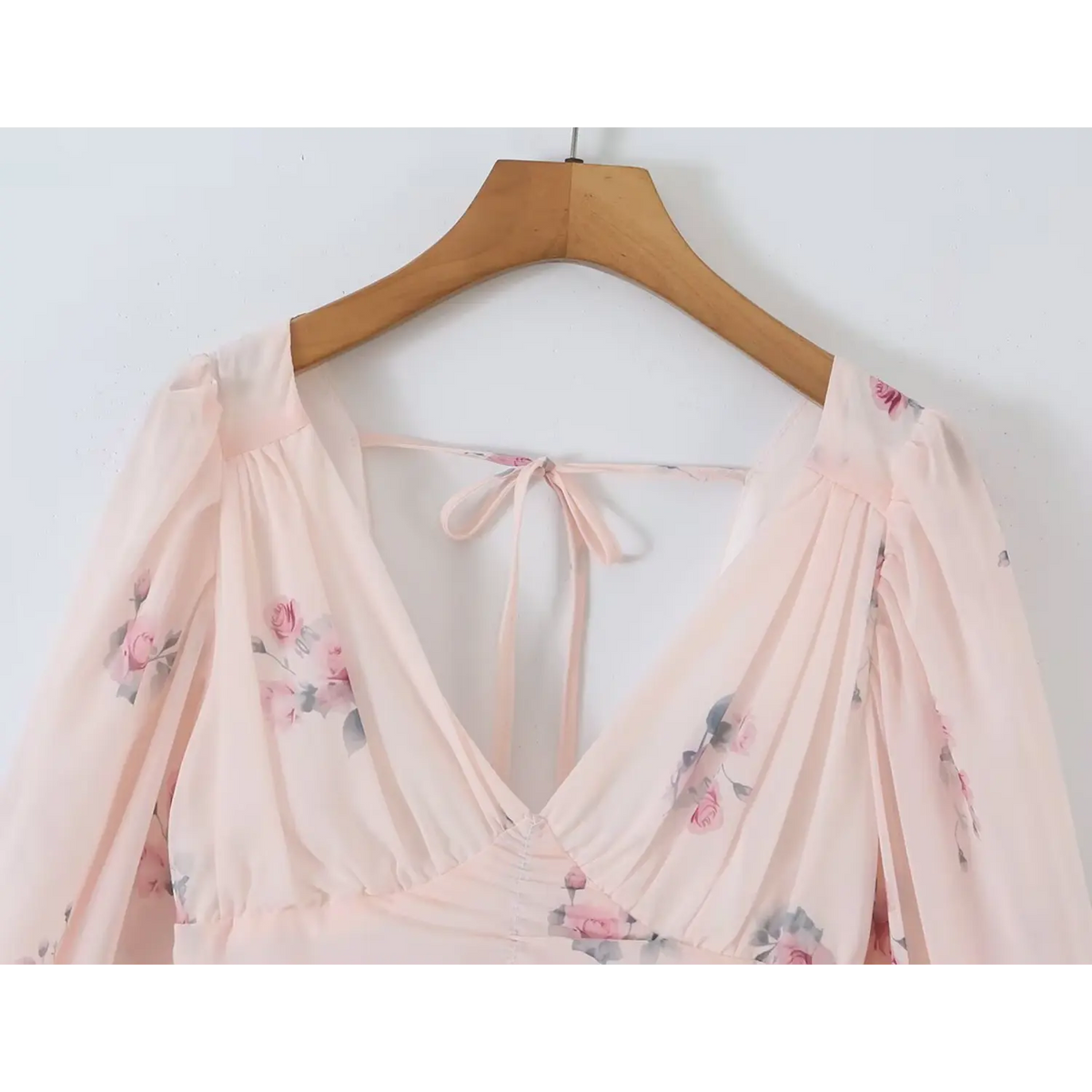 Soft pink floral chiffon dress hung on wooden hanger, deep v neck, gathered bust, long balloon sleeves and back tie detail