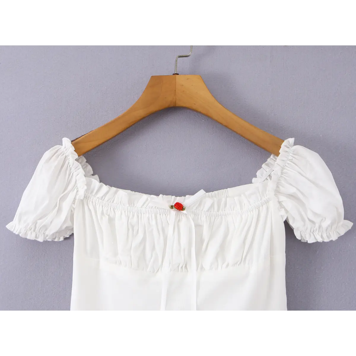 Close-up of the rose-accented ribbon bow on a white off-shoulder peplum top, highlighting the square neckline and ruffled trim.