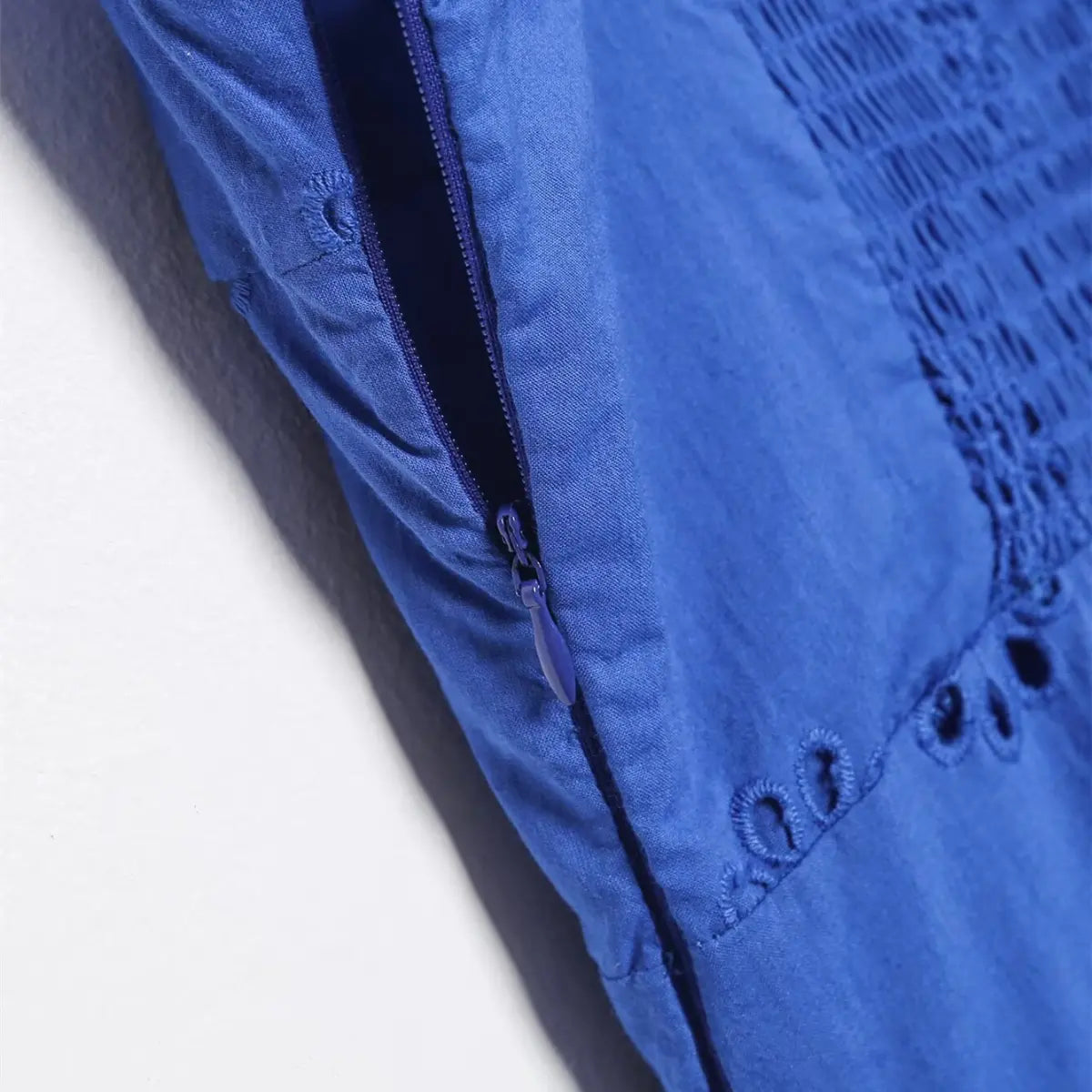 Close-up of the side zipper on the royal blue eyelet dress, featuring a matching blue zipper pull and stitched seam