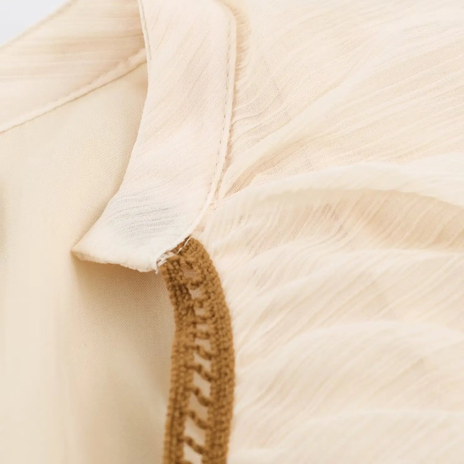 Stitching detail of ruffle edge with brown woven piping trim on beige dress