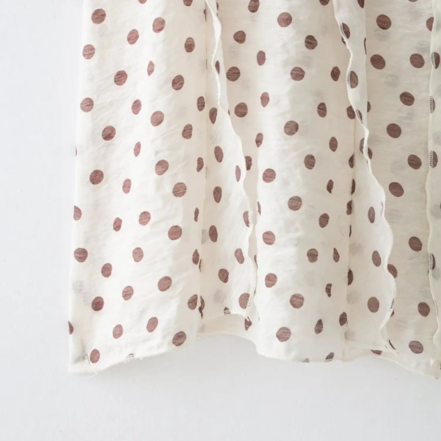 Close-up of layered wavy ruffle placket and uneven relaxed bottom hem on polka dot sleeveless shirt