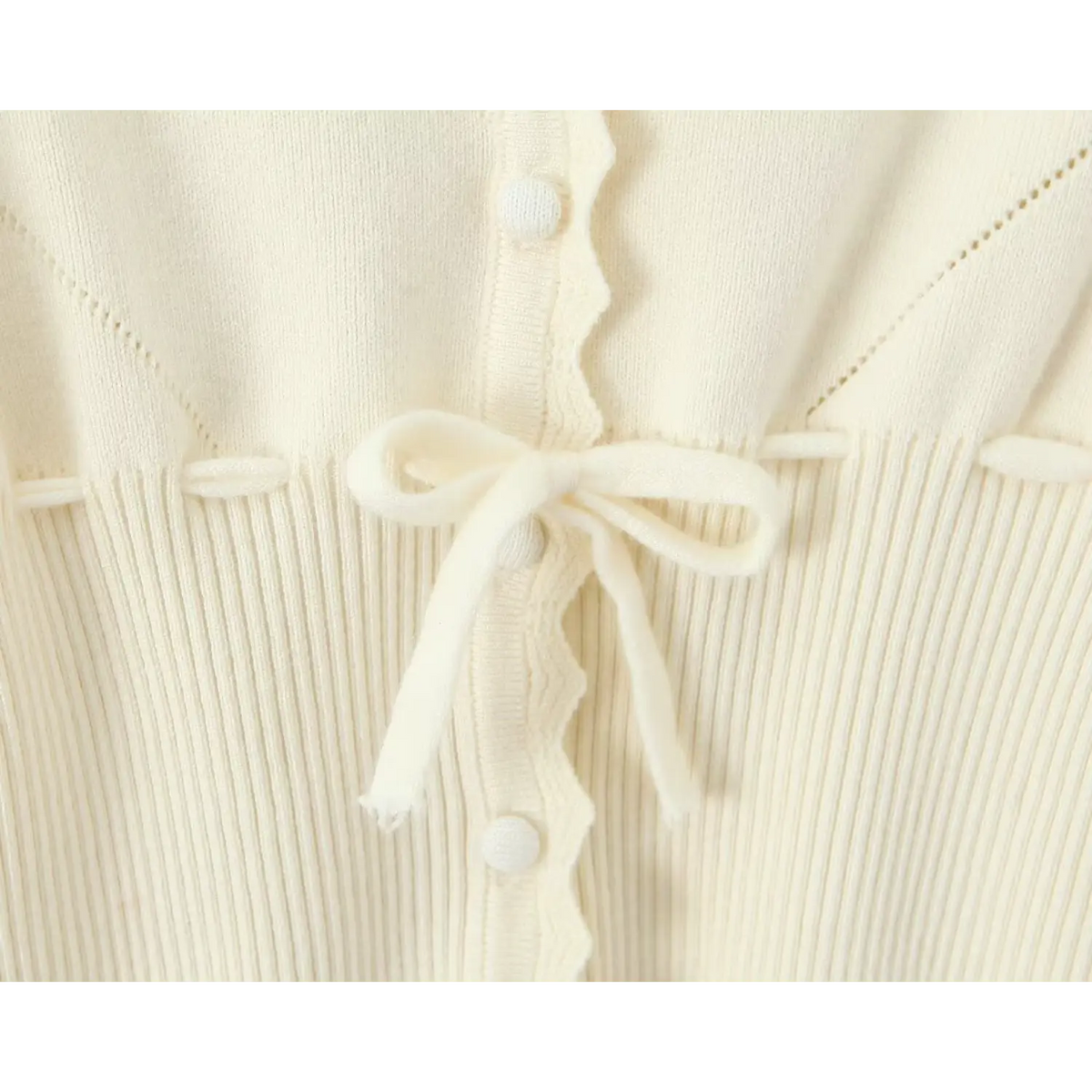 Close-up of knit bow tie and round knit button on ribbed fabric with scallop trim