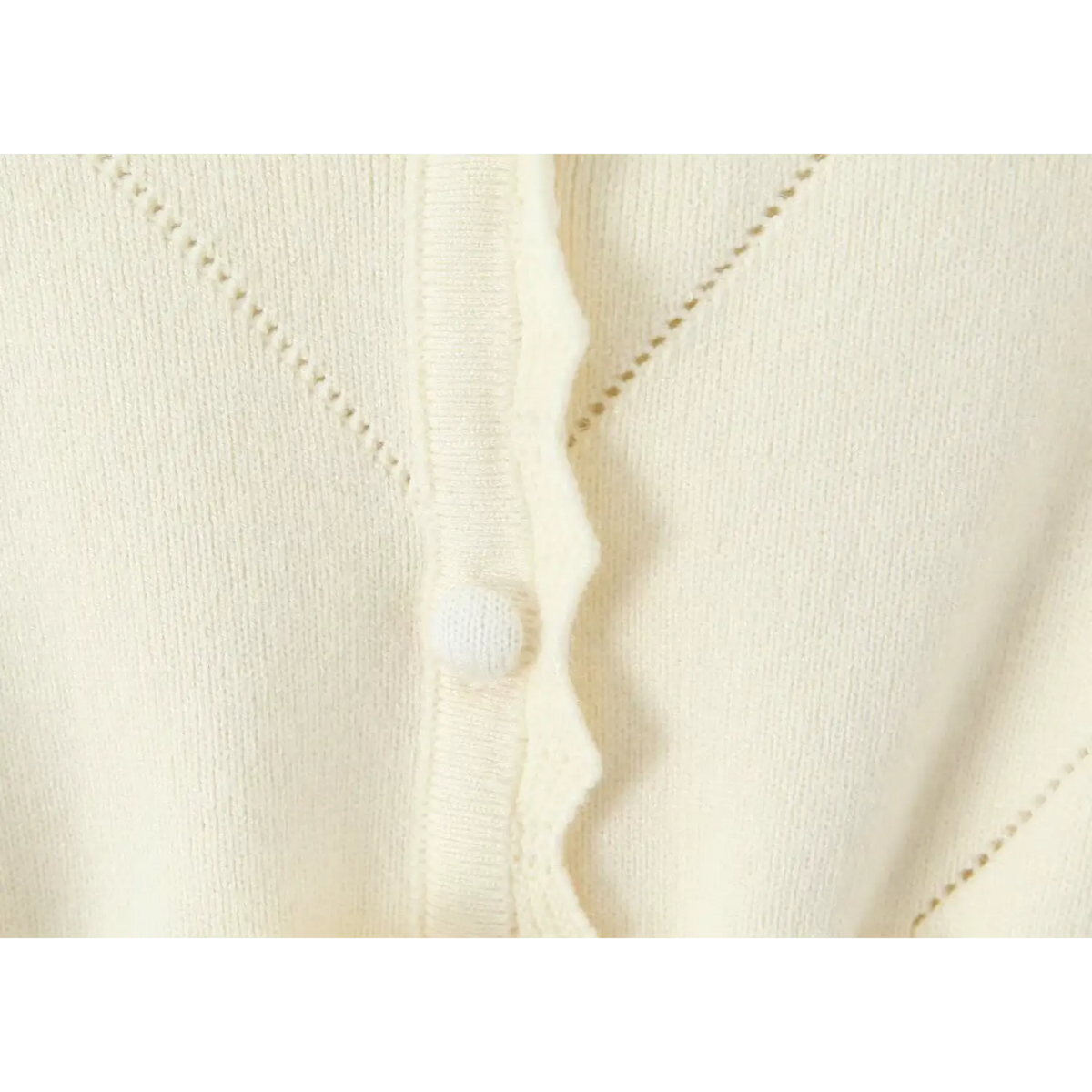 Close-up of ruffle edged placket with round knit button and diamond cutout stitching