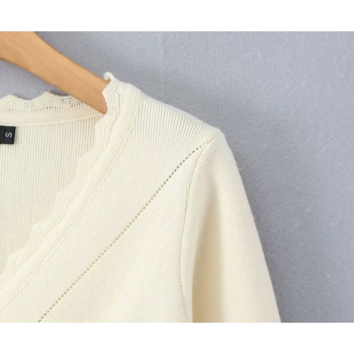 Close-up of ruffled V neck and shoulder on cream knit cardigan with size S label