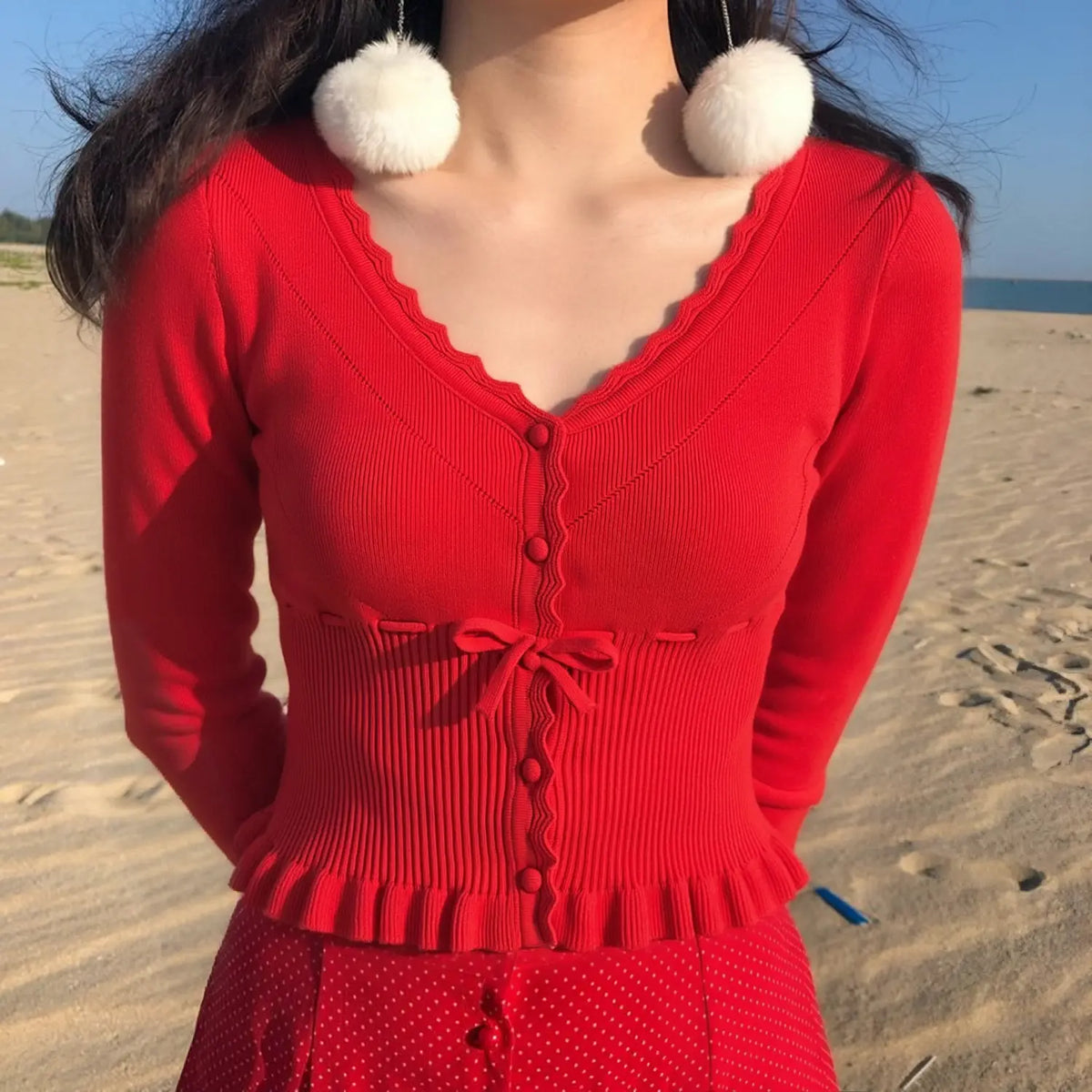 Model wearing red ruffle trim knit cardigan with polka dot skirt at the beach