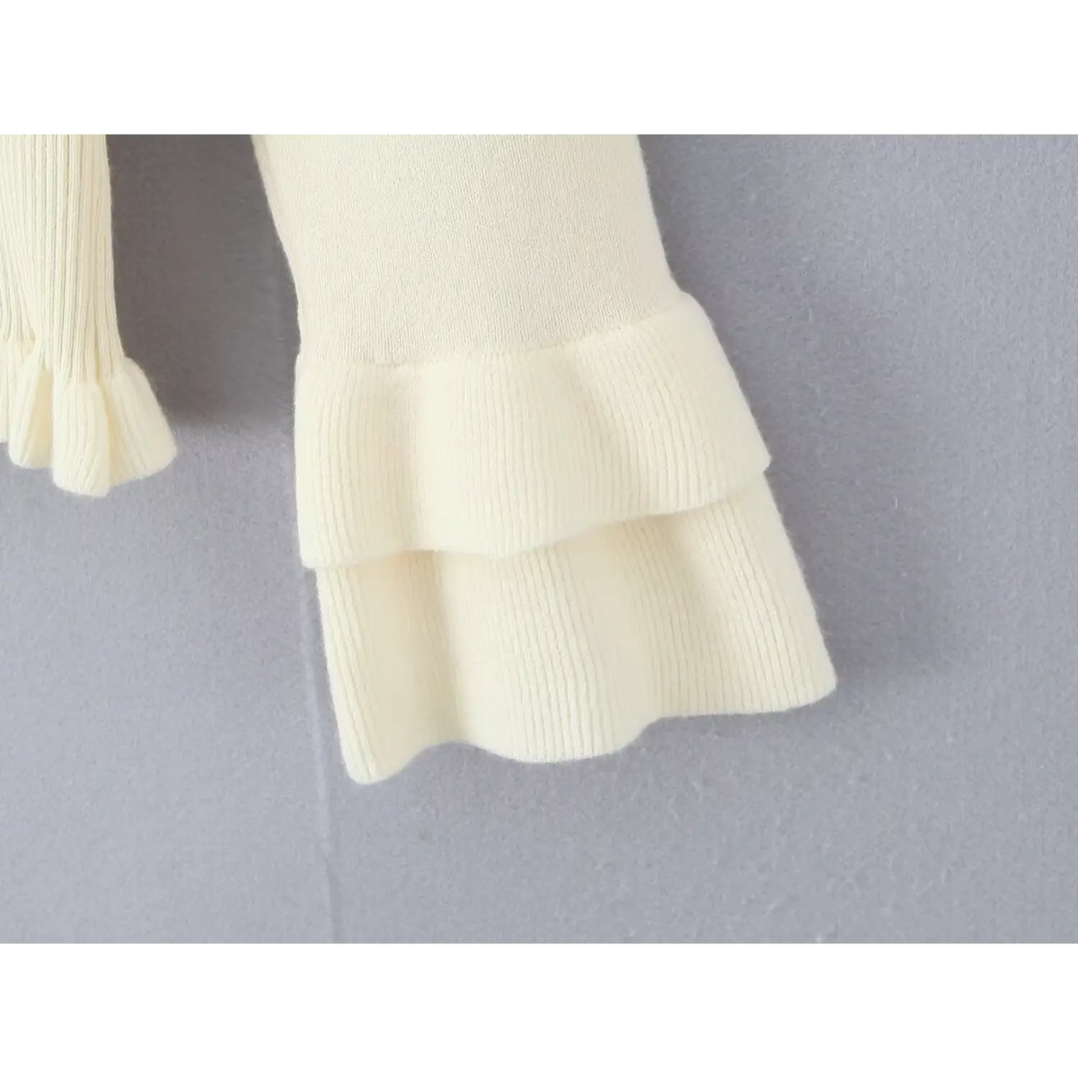 Close-up of double layered ruffled cuff on bell sleeve of cream knit cardigan