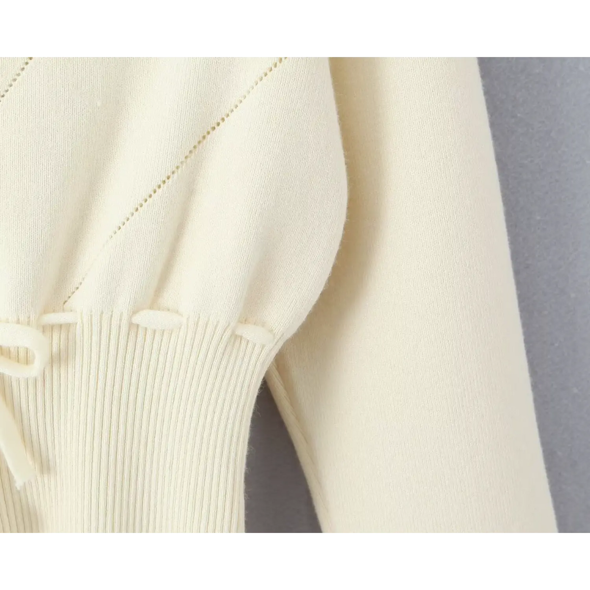 Close-up of shirred waistband and drawstring loops with diamond stitching on cream knit cardigan