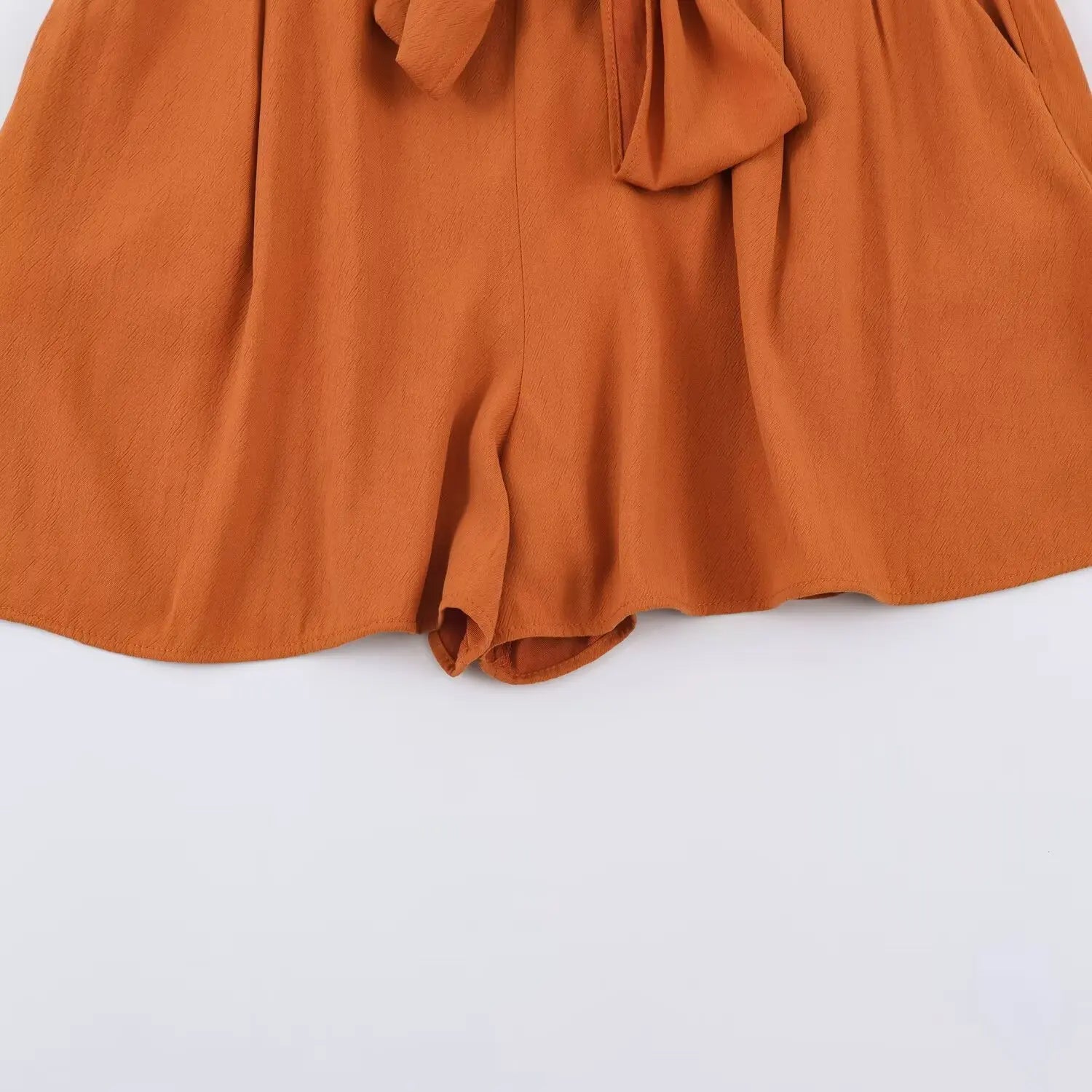 Partial shot of rust cowl neck romper wide shorts leg, relaxed gathered short pant hem, self fabric waist tie overlay
