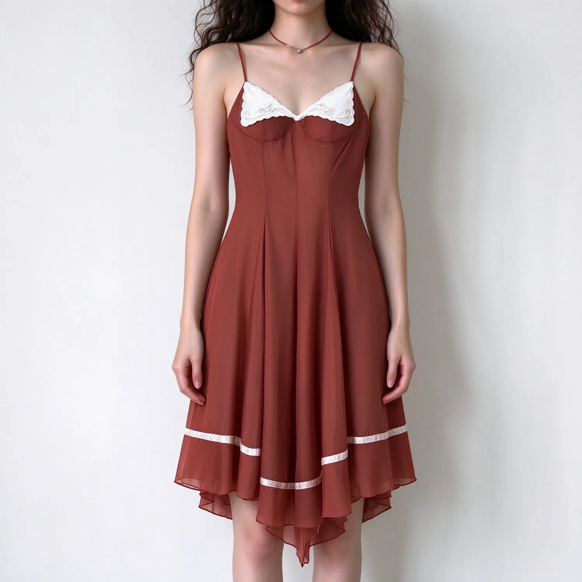 Model wearing rust spaghetti strap maxi dress with white lace bust trim and asymmetrical hem with ribbon detail, white background