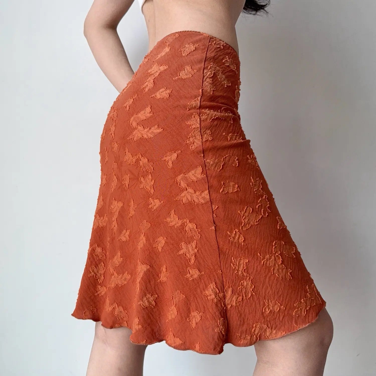 Side lifestyle shot on model of rust orange textured floral midi skirt, high waist, wavy hem, lightweight flared hem skirt
